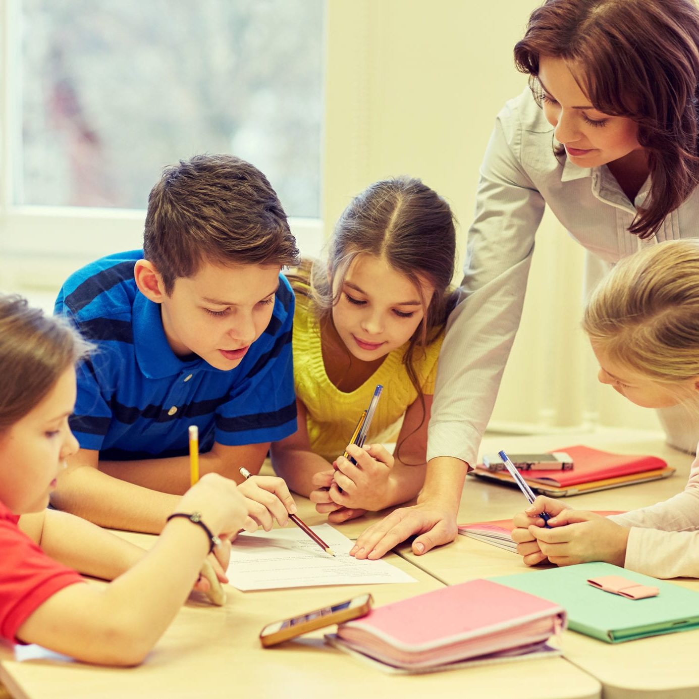 education, elementary school, learning and people concept - teacher helping school kids writing test in classroom